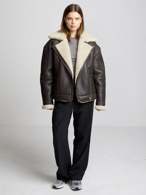 A model wearing a brown shearling jacket with a cozy collar, paired with black pants and sneakers, showcasing MEOTINE's stylish outerwear.