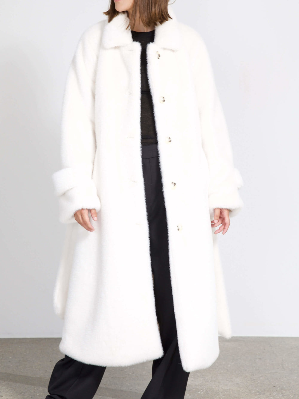 A model wears a cozy, oversized white MEOTINE coat, styled with black pants, showcasing a chic and modern look.