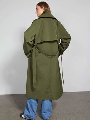 A model showcases a stylish olive green trench coat with a unique layered design and tied details, perfect for a chic look by MEOTINE.
