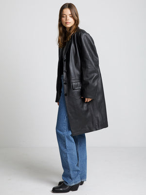 A model showcases a stylish black leather coat paired with high-waisted blue jeans, embodying a chic, modern look by MEOTINE.
