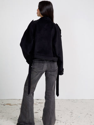 A model showcases a stylish black cropped jacket with a unique design, paired with flared gray jeans, representing MEOTINE's chic aesthetic.