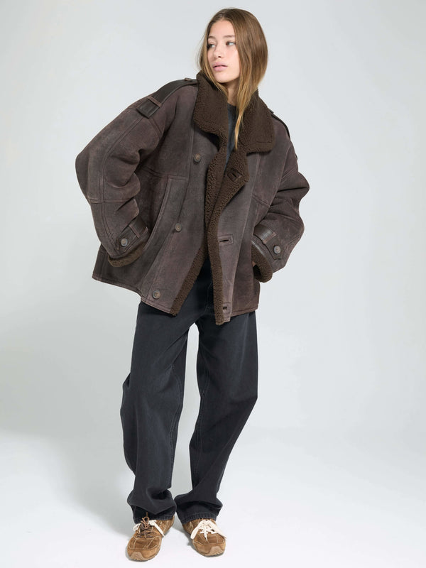 A model showcases a stylish oversized brown jacket with a cozy collar, paired with relaxed black pants and casual shoes. MEOTINE.