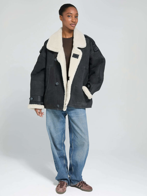 A model wears a stylish black MEOTINE jacket with a cozy white shearling collar, paired with relaxed blue jeans.