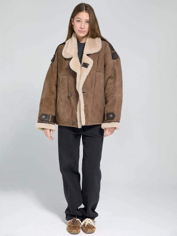 A model wears a stylish brown shearling jacket with a cozy collar, paired with black pants and casual shoes, showcasing MEOTINE's chic design.