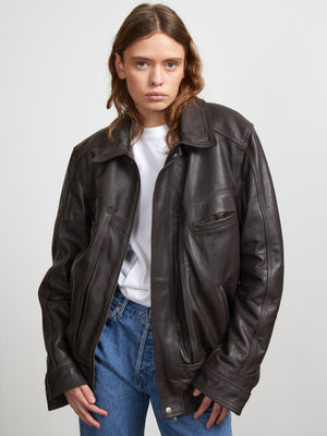 A model showcases a stylish brown leather jacket from MEOTINE, paired with a simple white t-shirt and blue jeans.