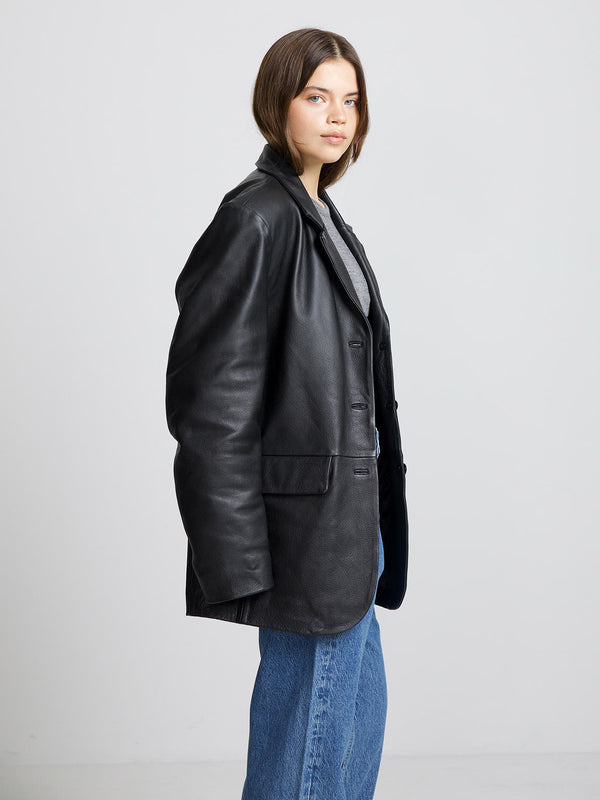 A model showcases a stylish black leather blazer from MEOTINE, paired with a casual gray top and blue jeans.