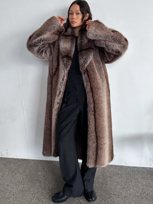 A model showcases a luxurious, oversized brown faux fur coat by MEOTINE, styled with black pants and a fitted top.